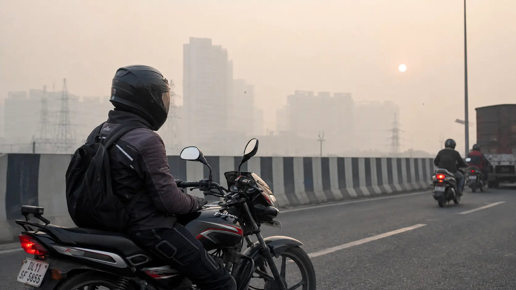 A rider idling on a flyover along the Delhi-Meerut Expressway, smog blurring the Ghaziabad skyline behind them, helmet visor down.