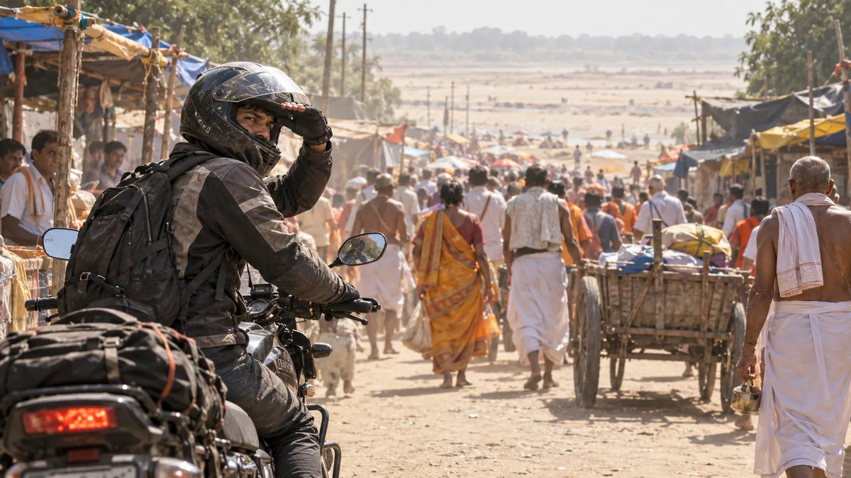 A rider astride his idling motorcycle glances back over his shoulder at a slow pilgrim procession behind him on a sandy Gaya lane, one hand shielding his eyes from heat glare.