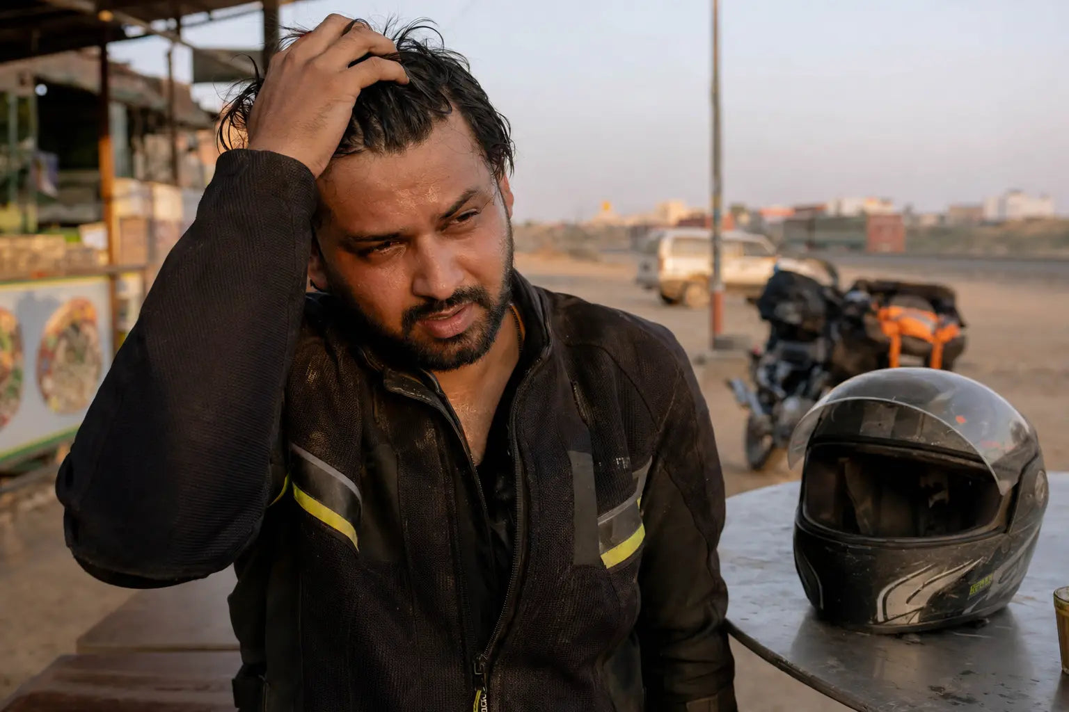 A rider running a hand through sweat-damp hair after pulling off a helmet at a roadside stop