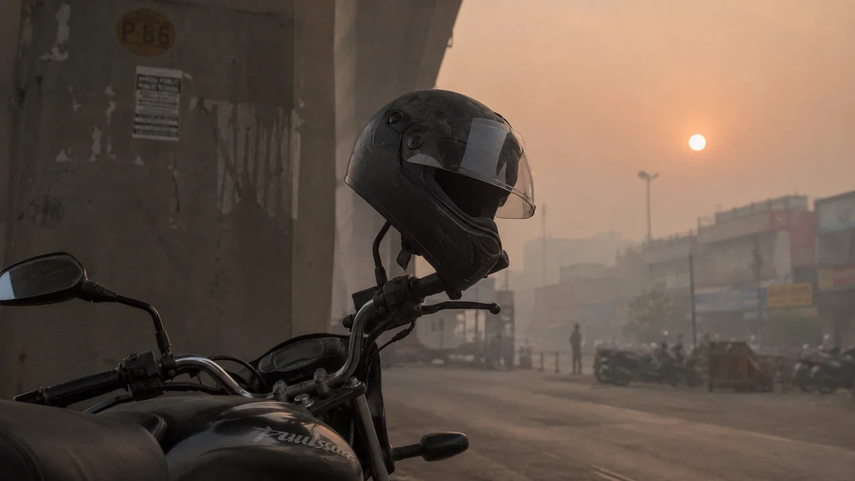 A parked motorcycle with a helmet resting on its mirror at a roadside in Delhi, a dull orange sun barely visible through thick winter smog behind a flyover pillar.