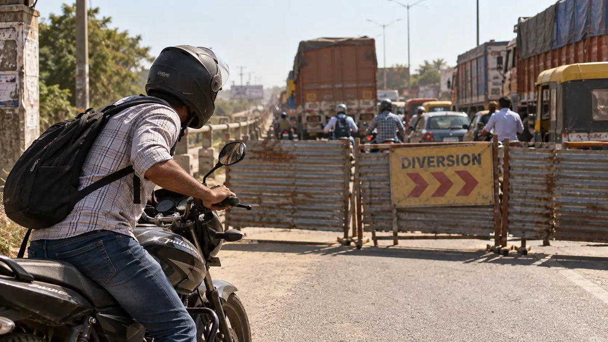 A rider stopped at a barricade on the closed Vikramshila Setu approach road near Bhagalpur, leaning to look past a stalled truck queue under a flat overcast sky.