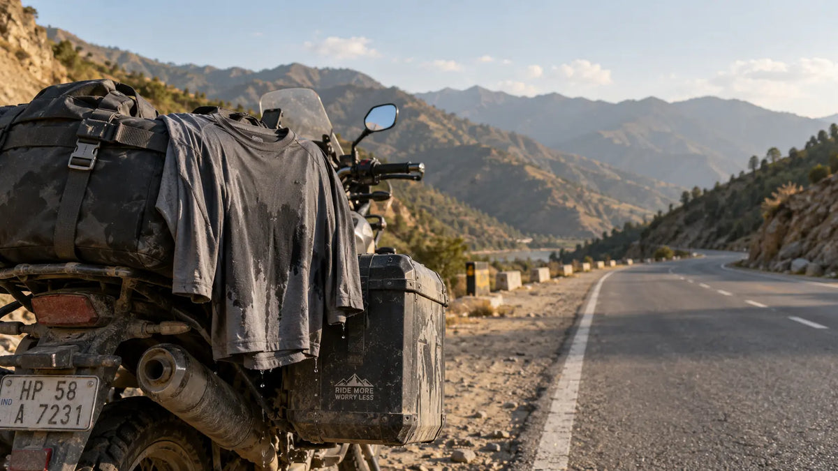 A damp riding base layer clipped to a motorcycle's luggage strap, drying in late-afternoon light on an open mountain highway.
