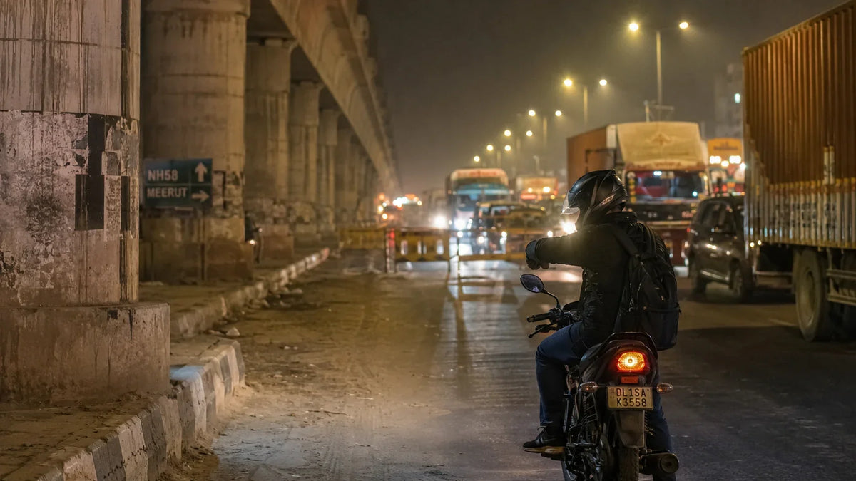 A rider on a motorcycle waits under sodium streetlights beneath the raised Namo Bharat RRTS viaduct near Meerut at night.