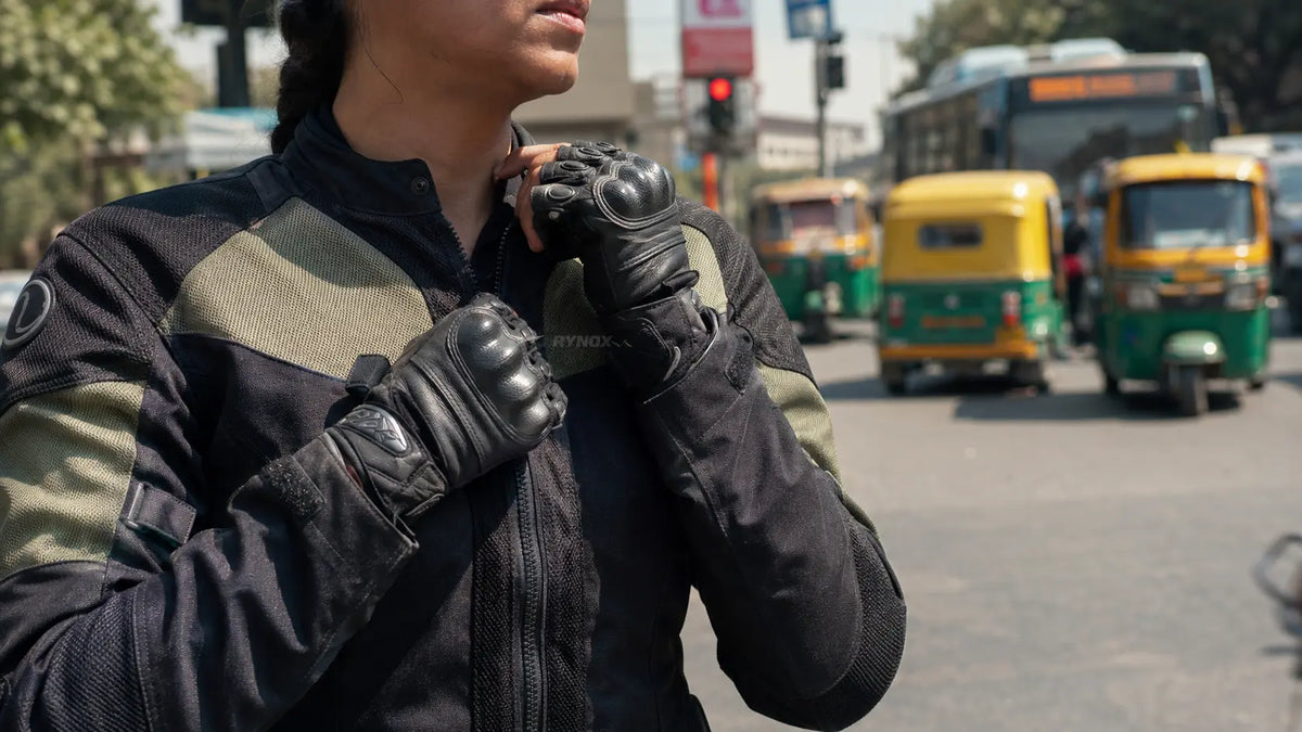 A woman rider adjusts the collar zip of her riding jacket at a midday traffic stop, hands visible on the fabric.