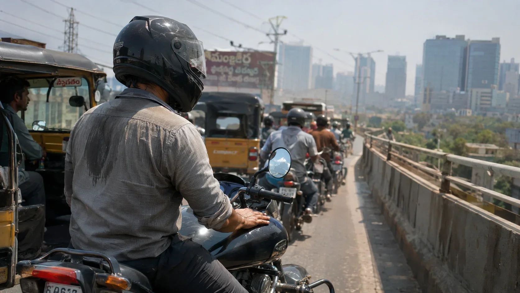 Rider seated on a motorcycle at a standstill on a Hyderabad flyover, helmet on, heat haze rising off the road with distant IT tower skyline behind.