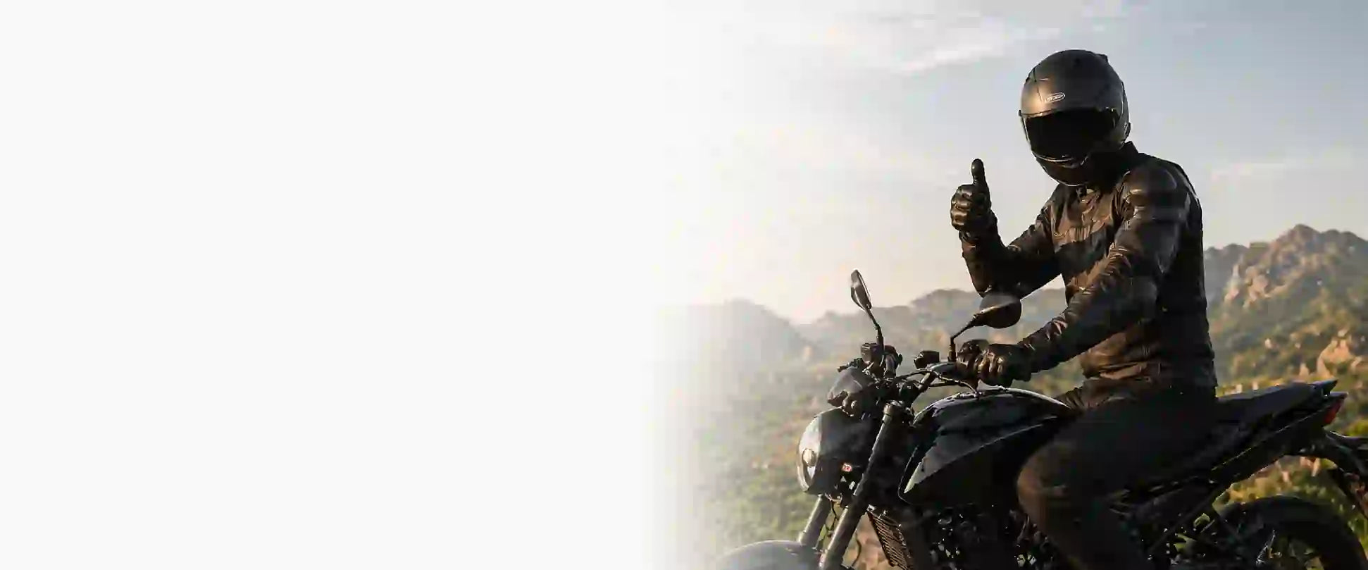 Person on a motorcycle giving a thumbs-up gesture with mountains in the background